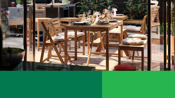 Outdoor dining area with wooden table and chairs set with dishes and plants nearby.