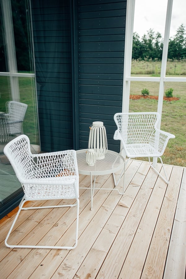 Outdoor patio with white wicker chairs and round table – Minimalist terrace setup with two white woven chairs, matching round table, and decorative lanterns on wooden decking.