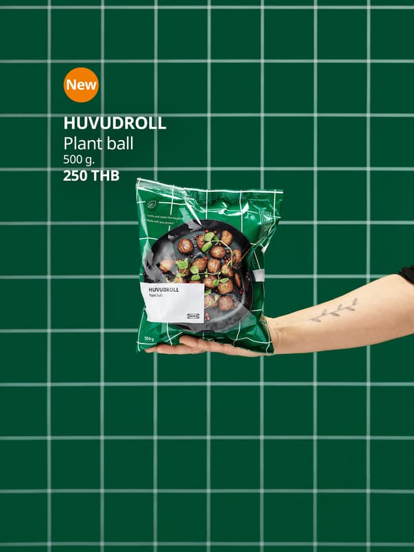 Outstretched hand holding an unopened package of HUVUDROLL plant balls. Green, tiled wall in the background.