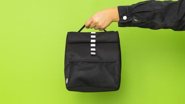 outstretched hand holds black lunchbag against green background
