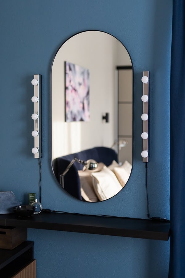 Oval mirror with vanity lights on blue accent wall in modern bedroom interior