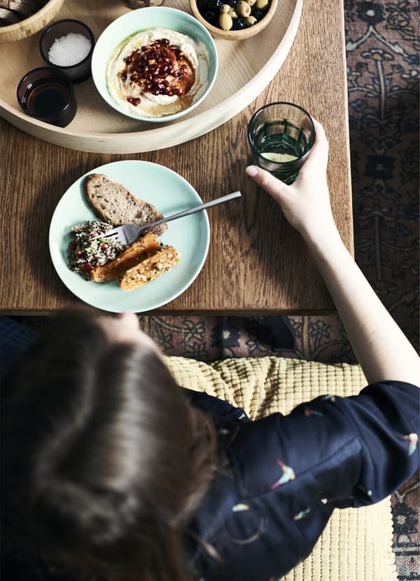 Overhead view of a person eating Moroccan-style food from a turquoise plate set at a wooden table.