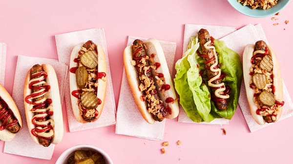 Overhead view of a row of KORVMOJ Vegetable hot dogs with various toppings including ketchup, mustard, pickles, and fried onions