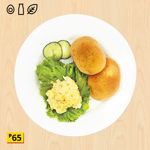 Overhead view of a white plate with two golden breaded patties, lettuce, cucumber slices, and creamy salad on a light wood table.