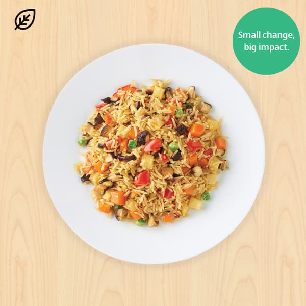 Overhead view of colorful vegetable fried rice on a white plate over wood, with a green “Small change, big impact” badge promoting sustainability.