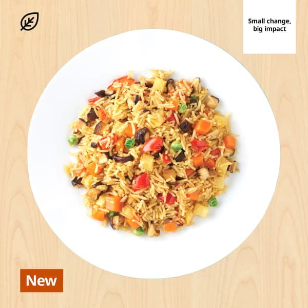 Overhead view of colorful vegetable fried rice on a white plate over wood, with a green “Small change, big impact” badge promoting sustainability.