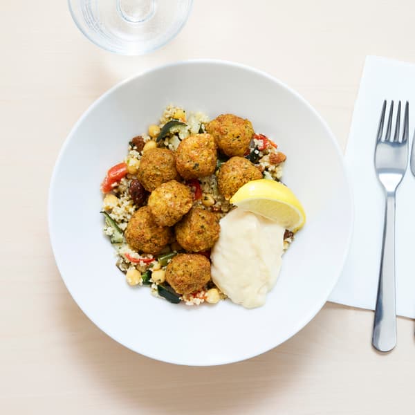 På ett bord står en vit tallrik med falafel och couscous. Bredvid ligger en gaffel på en servett. 