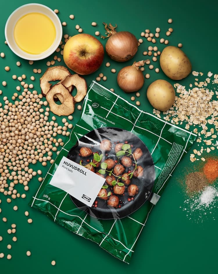 Package of HUVUDROLL plant balls, surrounded by the unprocessed ingredients: peas, oats, potatoes, onions, apples and spices.