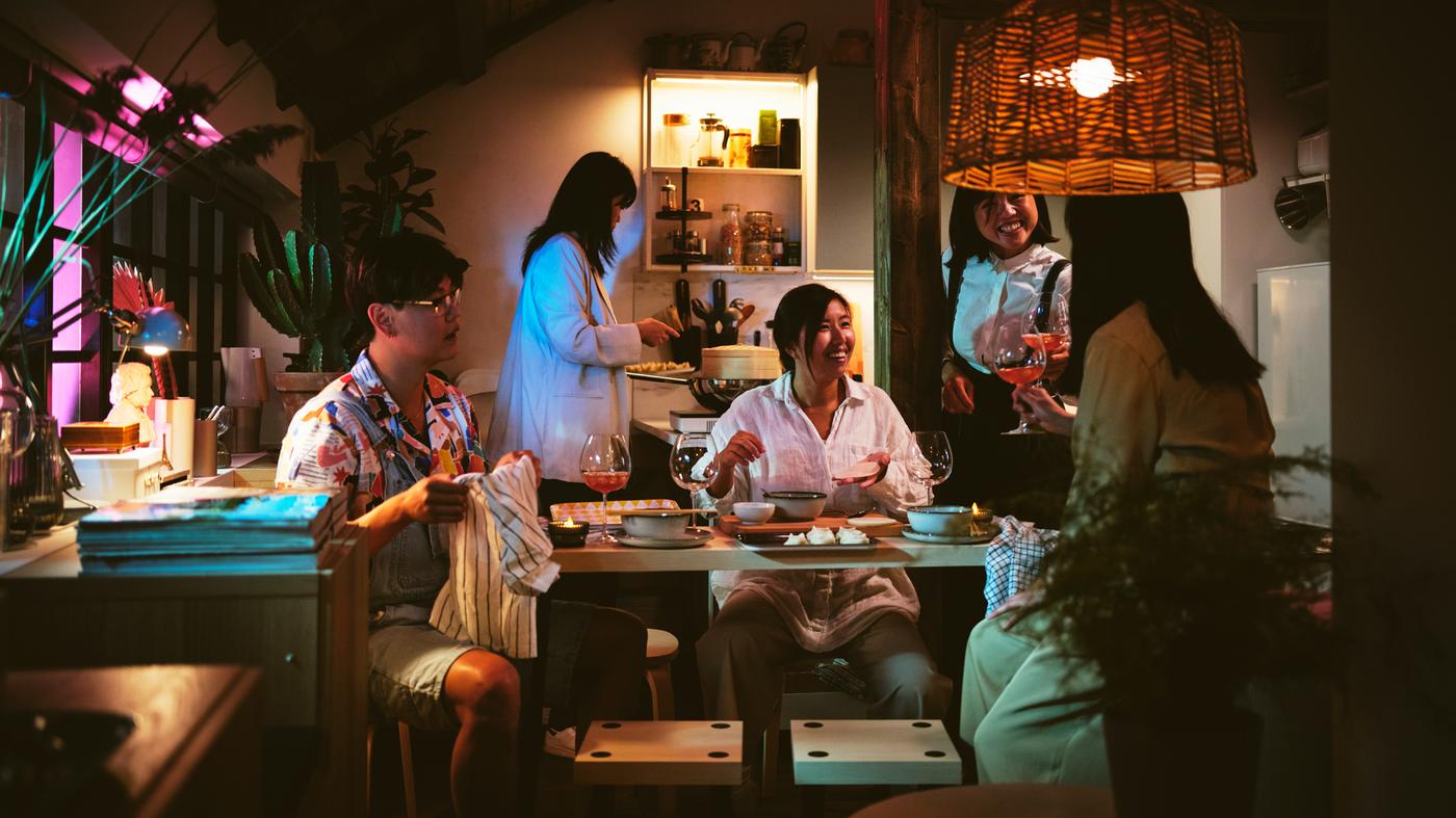 Päť ľudí okolo súpravy 4 stolíkov a stoličiek FRIDNÄS s čiernymi prvkami a brezovým vzorom. Nad nimi je závesná lampa s tienidlom KAPPELAND.