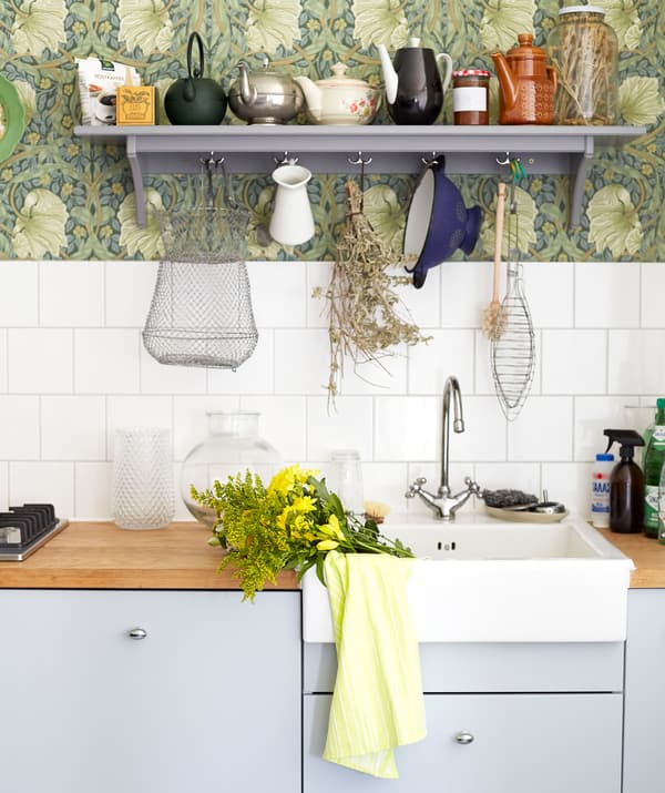 Pale gray kitchen cupboards, wooden worktops and a white sink, with white tiles and a gray shelf above.