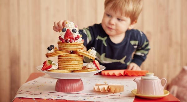 Pancake cake with berries and child reaching for it.