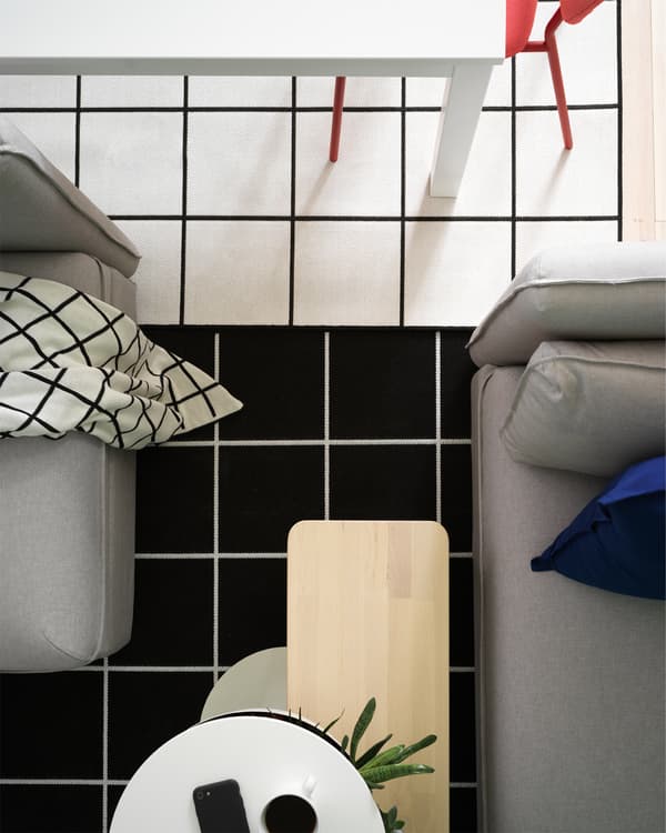 Pandangan dari atas yang membolehkan anda melihat dua ambal corak segi empat sama berwarna hitam putih, meja makan berwarna putih dan sofa berwarna kelabu.