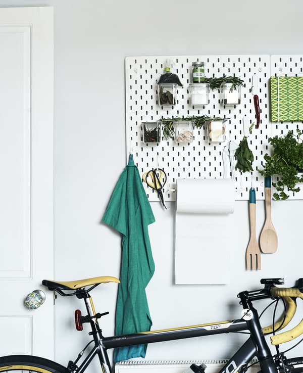 Panneau perforé blanc garni d’outils et de plantes, dans une pièce blanche.
