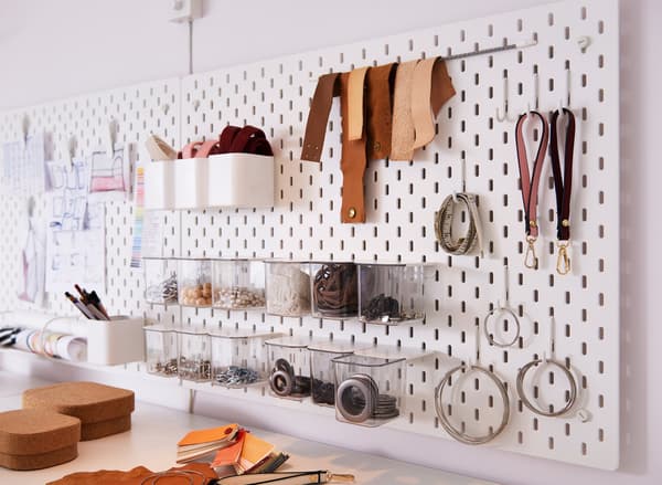 Panneau perforé blanc IKEA SKÅDIS pour le rangement d’accessoires et d’autres objets, avec des cordons, des crochets et des récipients transparents en option.
