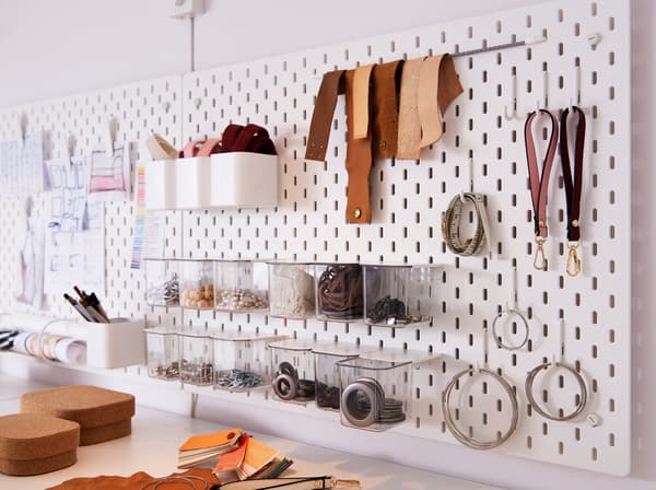 Panneau perforé SKÅDIS blanc doté de crochets, de cordons élastiques et d’autres récipients qui accueille des fournitures de bureau. 