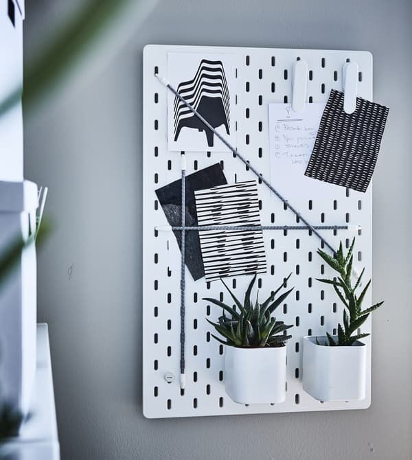 Panneau perforé SKÅDIS installé au mur, plantes et papiers y trouvent leur place.