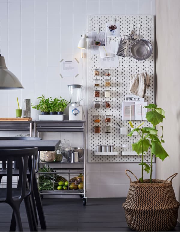Panneaux perforés blancs SKÅDIS fixés à un mur de cuisine, à côté d’un plan de travail, avec support pour livre de recette et boîtes pour ingrédients à smoothies.  