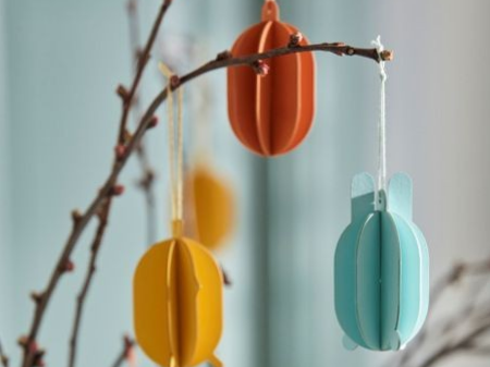 Pappersdekorationer i form av ägg hänger på grenar i påskris.