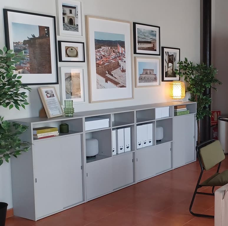 Pared decorada con marcos de fotos y un mueble gris con carpetas organizadoras.