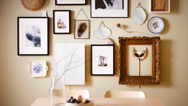 Parede com quadros por cima de uma mesa RÖNNINGE em freixo, com molduras RIBBA e LOMVIKEN em preto e outras molduras e artigos decorativos.