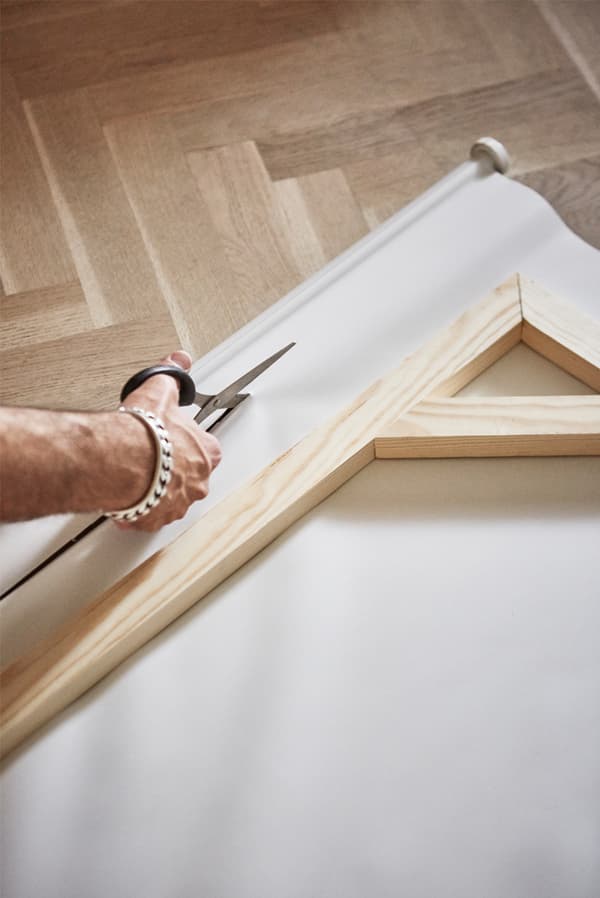 Parquet wooden floor with man cutting a canvas window blind with scissors and a wooden picture frame on top of the canvas.