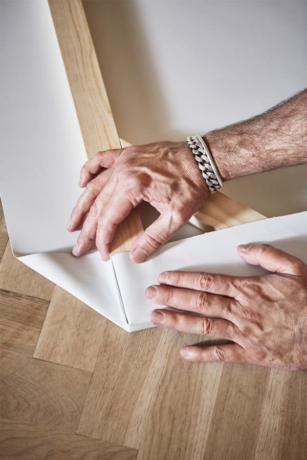 Parquet wooden floor with man’s hands folding a piece of white canvas onto the corner of a wooden picture frame.