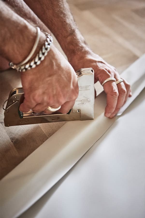 Parquet wooden floor with man’s hands stapling a piece of white canvas to a wooden picture frame with a staple gun.