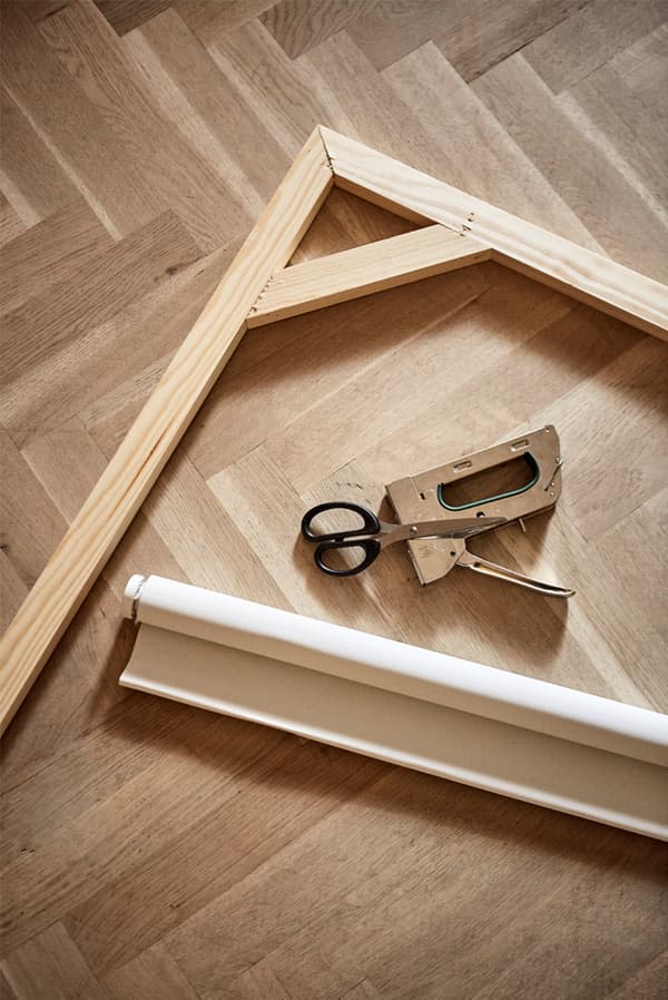 Parquet wooden floor with wooden picture frame, rolled up canvas window blind, staple gun and pair of scissors.