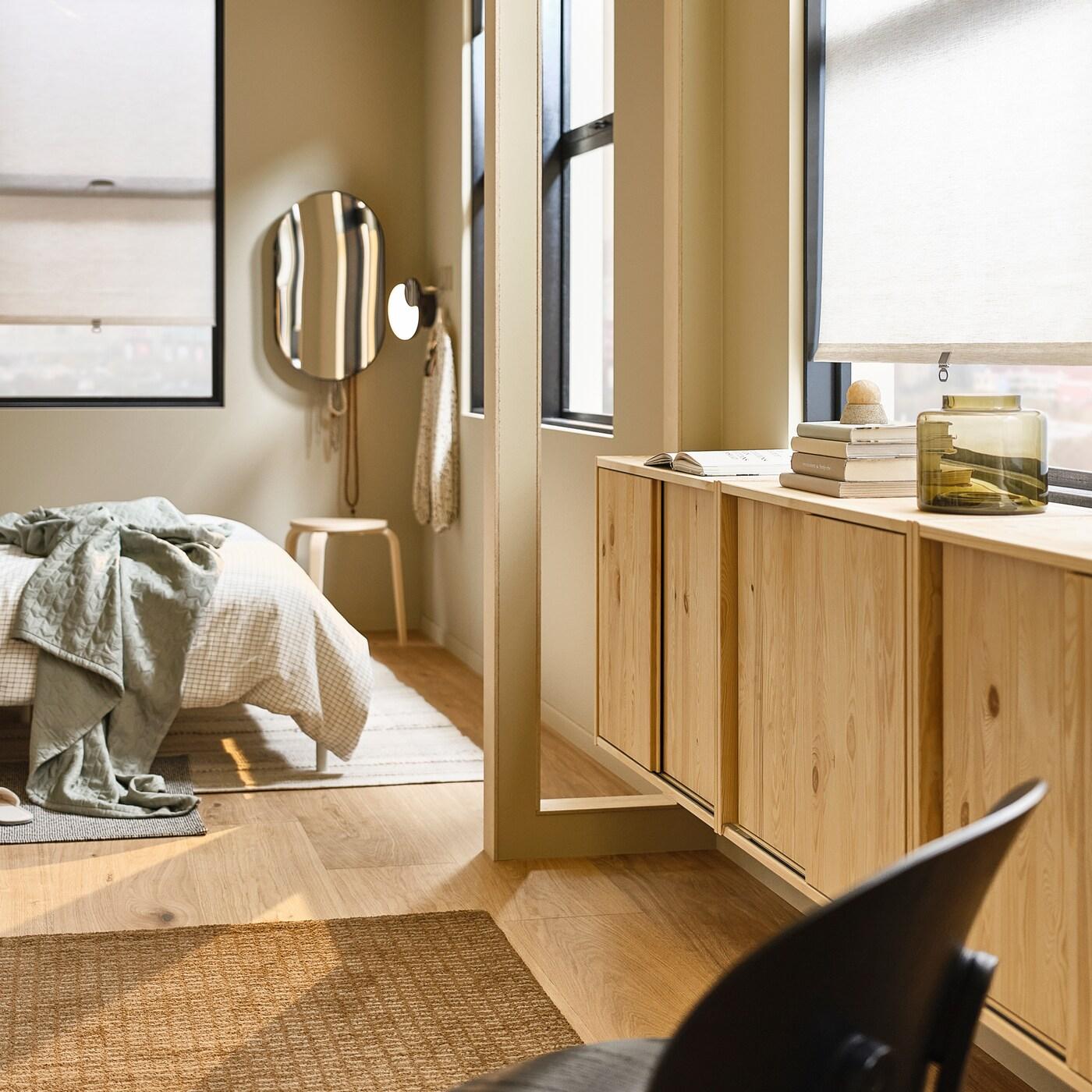 Part of a light, softly sunlit bedroom with IVAR pine cabinets with sliding doors wall-mounted beneath a row of windows.