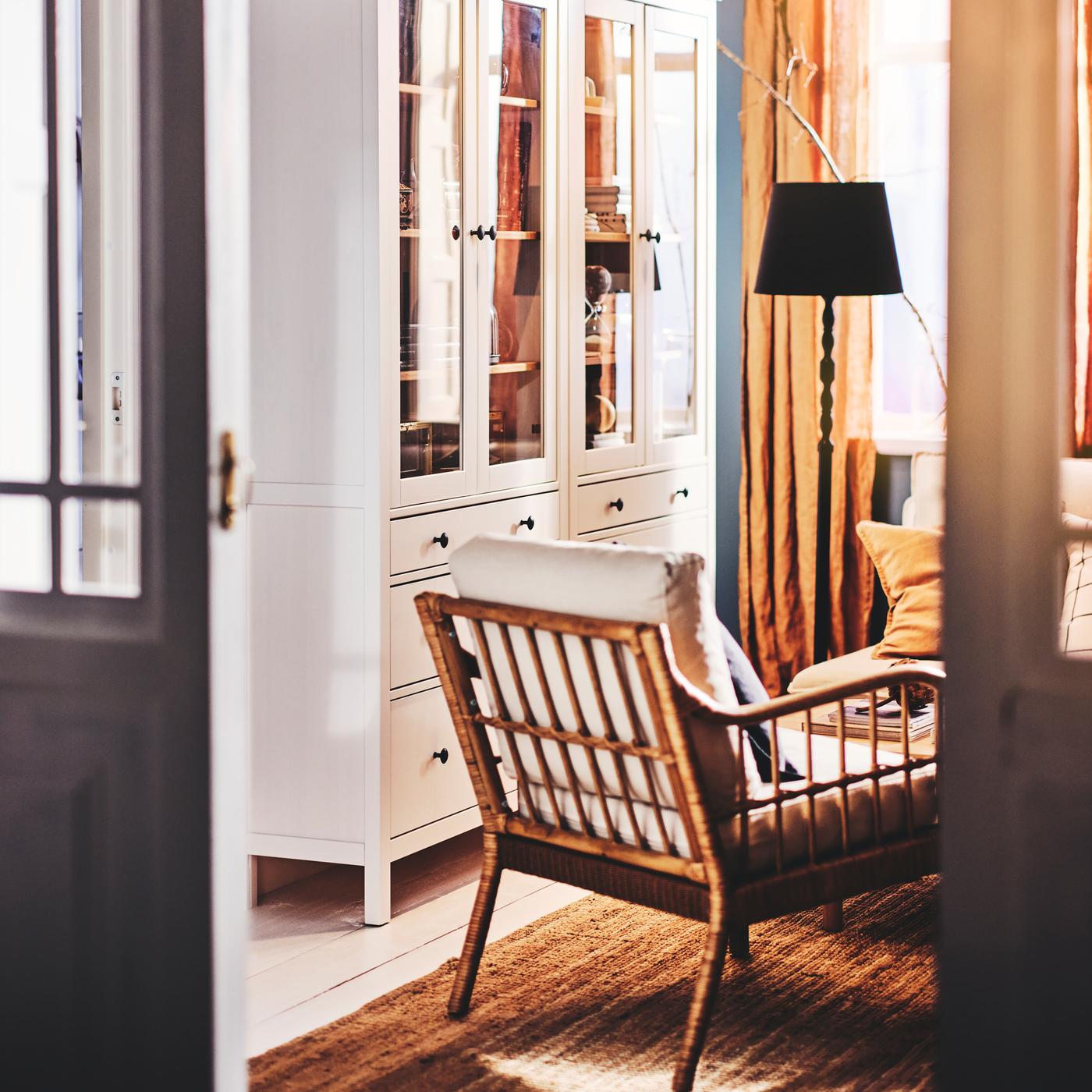 Part of a living room with two white HEMNES glass-door cabinets with three drawers, and an armchair on a rug.
