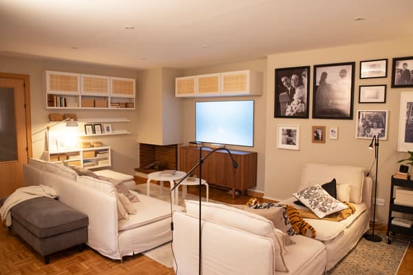 Parte de salón dividida por sofás blancos, con espacio de almacenaje, cuadros y diferentes elementos de decoración.