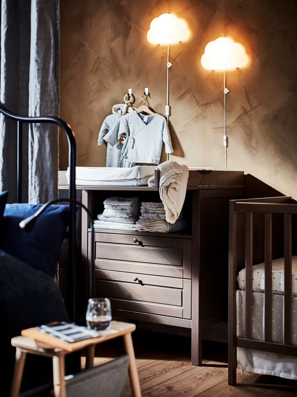 Parte de um quarto, parcialmente oculta por trás de um cortinado que divide o espaço, com um berço de bebé e um trocador SUNDVIK.