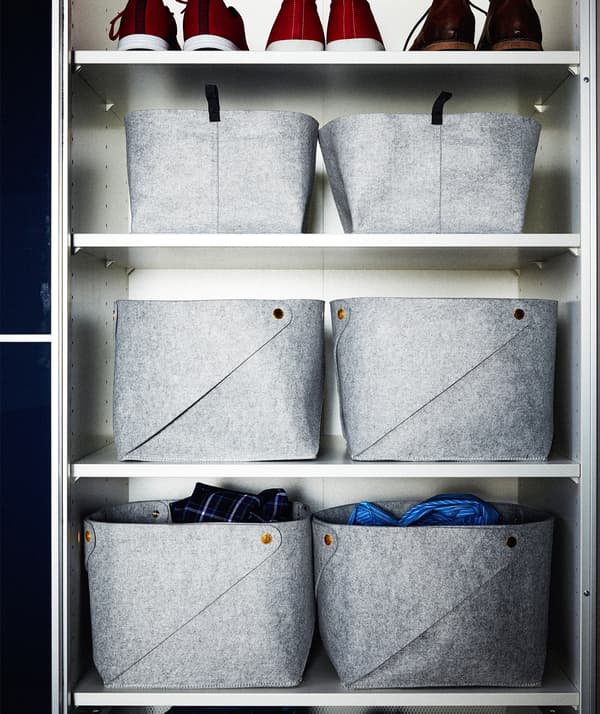 Parte de um roupeiro dividido por prateleiras em compartimentos individuais, cheios com cestos de feltro em forma de cubo e uma fila de sapatos.