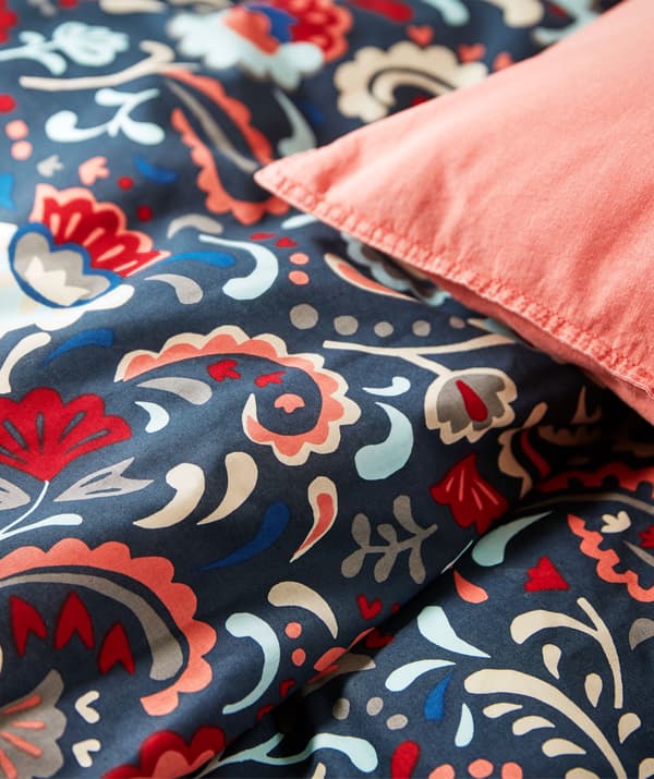 Parte de uma cama com roupa de cama em cores vivas e decorada com um padrão sueco tradicional com cornucópias.