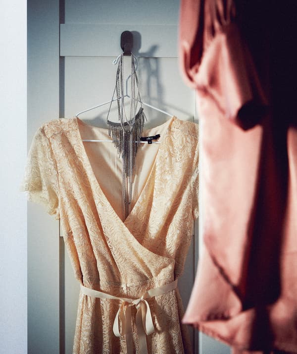 Parte de uma porta de roupeiro aberta com um gancho, onde está pendurado um cabide com um colar e um vestido de festa sem mangas.