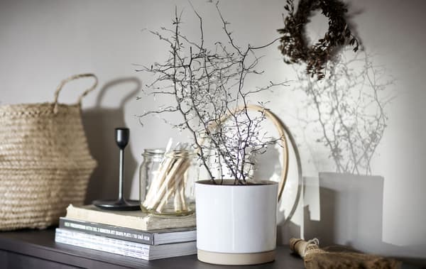 Parte superior dun aparador con diferentes obxectos decorativos, almacenamento á vista, cesta de ratán, libros, candeeiro e testo cunha planta.