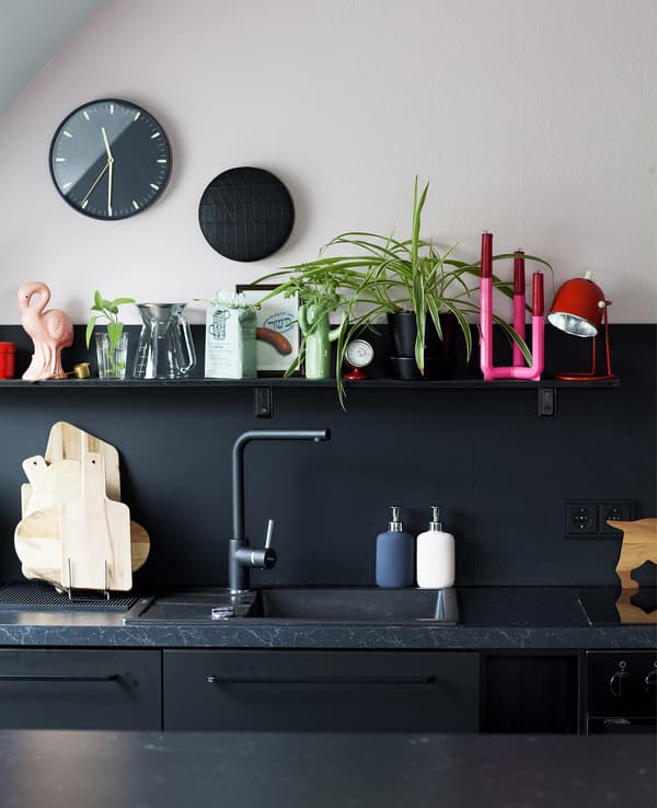 Partie de cuisine en noir et rose, avec étagère au-dessus de l’évier.