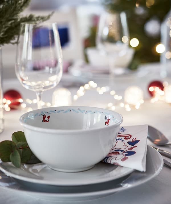 Partie de table décorée pour la fête. Assiettes multiples, guirlandes lumineuses sur la table, décorations avec verdure d’hiver, verre à vin.