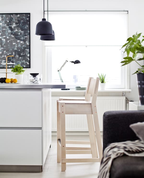 Partie d’îlot de cuisine blanc, avec tabouret en bois clair.