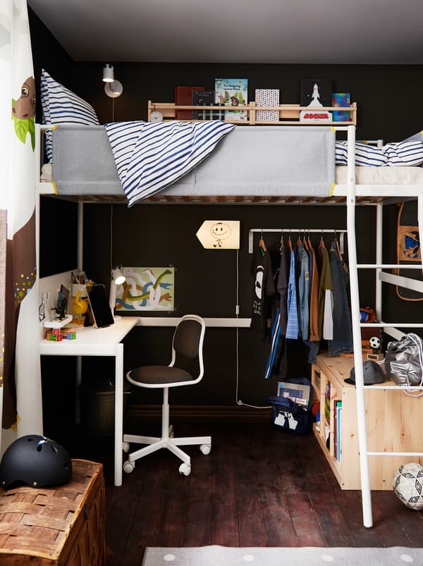 Partie d’une chambre d’enfant composée d’un lit mezzanine VITVAL avec un coin bureau installé en dessous, des vêtements sur des cintres et un espace de rangement.