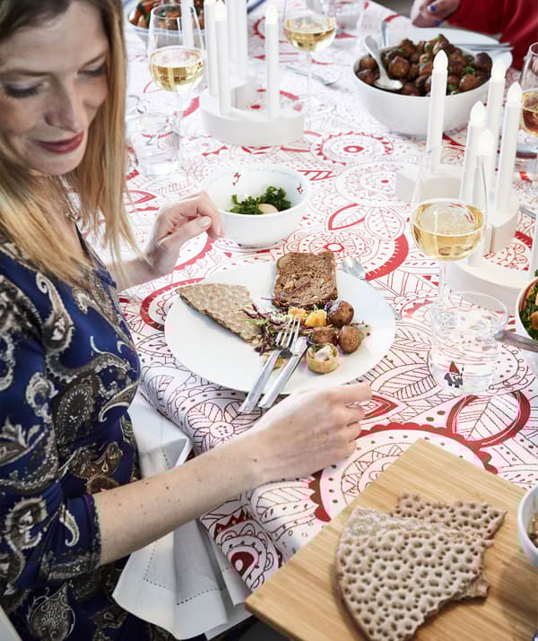 Partie d’une table décorée pour la fête avec nourriture, boissons et des gens. Une femme se voit offrir un plateau avec du pain croustillant.