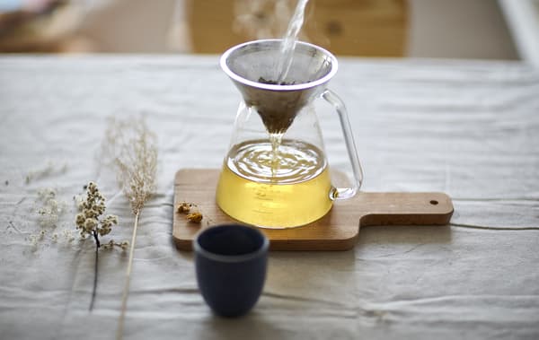 Passoire à thé déposée sur une tasse en verre, le tout sur une planche à découper en bois.