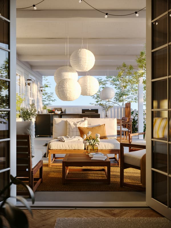 Patio visto dall'interno di una stanza, con set a 4 posti da giardino NÄMMARÖ sul quale sono appese lampade a sospensione a LED SOLVINDEN a energia solare.