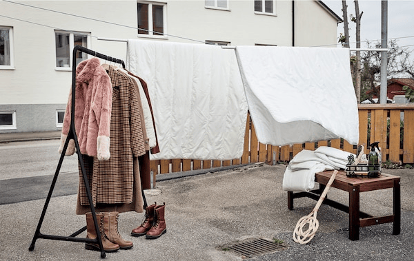 Paved front garden set up for spring clean: duvets hanging from lines, a clothes rack, shoes, textiles, cleaning accessories.