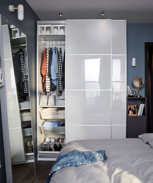 ห้องนอนขนาดเล็กที่ใช้ส่วนหนึ่งของผนังเป็นตู้เสื้อผ้า PAX/พักซ์ เต็มพื้นที่ บานตู้เปิดไว้ให้เห็นสิ่งของที่จัดไว้อย่างเป็นระเบียบ และตู้ทรงแคบ