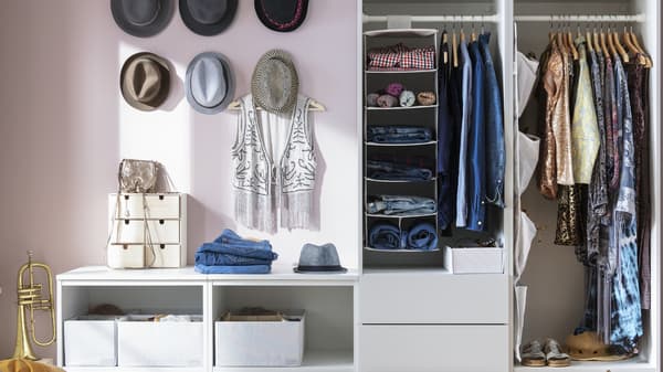 PAX wardrobe in bedroom with pink walls, showing neatly organised clothing items on the right hanging on BUMERANG hangers and a SKUBB clothes organiser on the left with clothing items neatly folded. 
