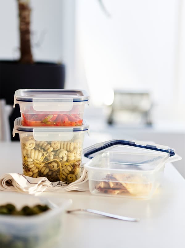 Pe un blat de lucru se află recipiente alimentare IKEA 365+ de diferite dimensiuni, cu diferite amestecuri de paste și legume.