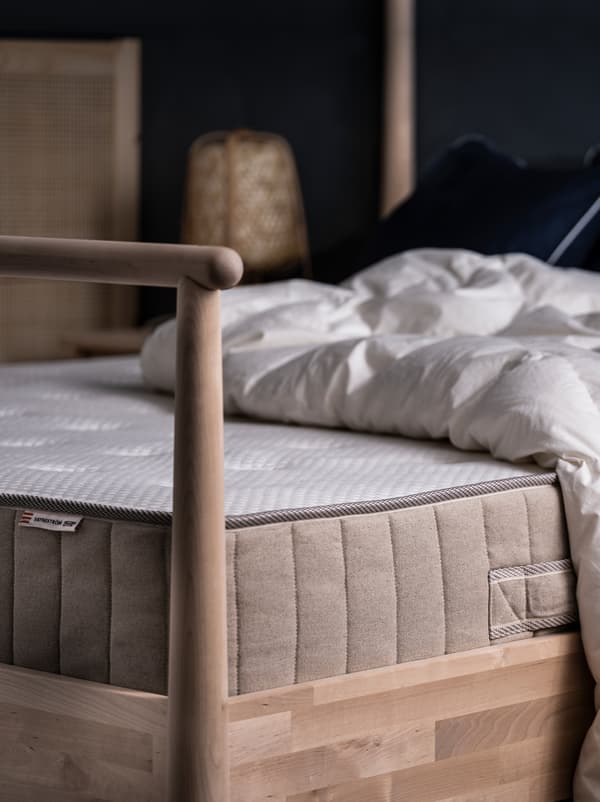 Pe un pat GJÖRA din lemn de mesteacăn aflat într-un dormitor luminat subtil se află o saltea VATNESTRÖM și o pilotă, ambele fără lenjerie de pat.