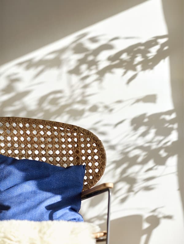 Peau de mouton et coussin bleu posés sur un fauteuil à bascule en rotin.