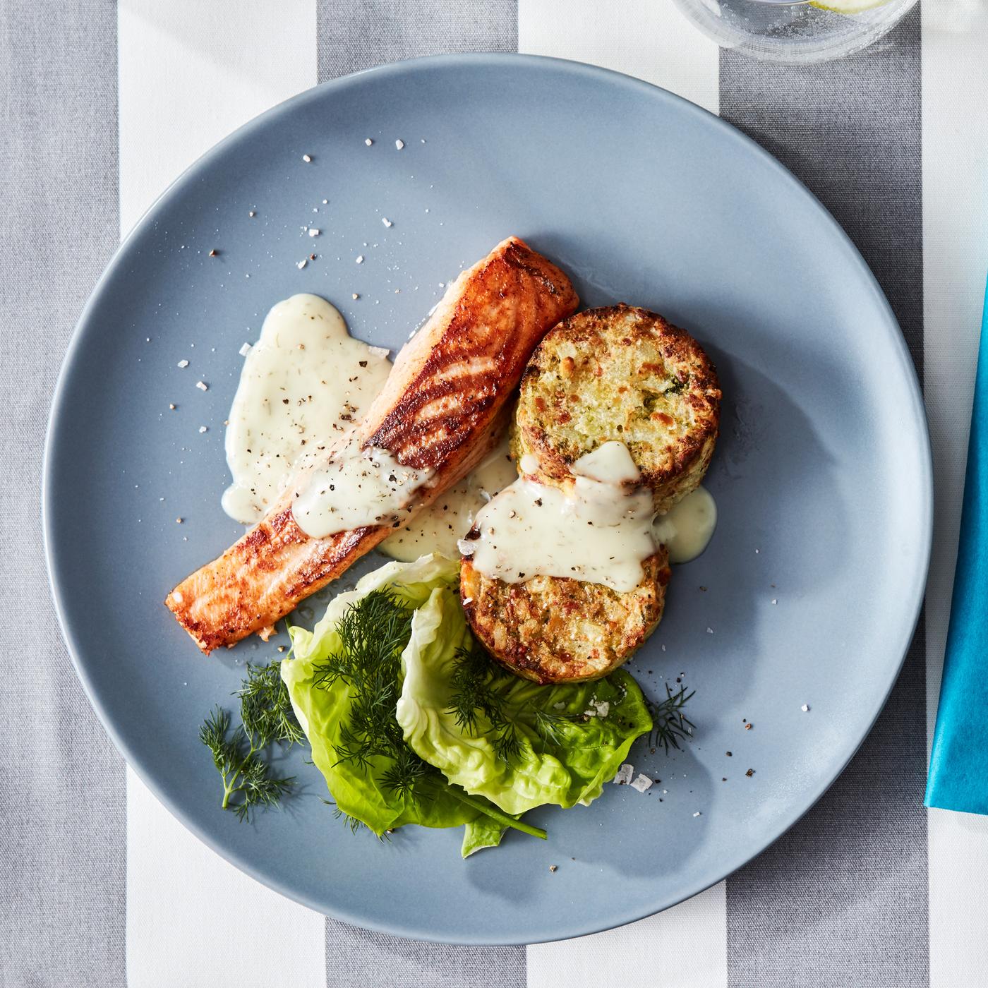 Pečeni losos s umakom, dvije popečke od povrća, zelena salata i kopar na plavom tanjuru.
